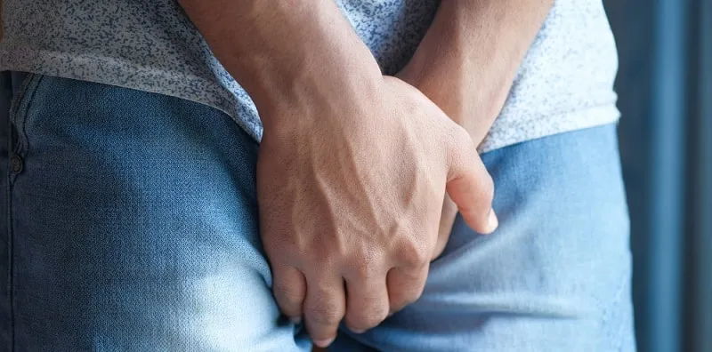 Man holding his lower abdomen, a common sign of prostate related urinary discomfort